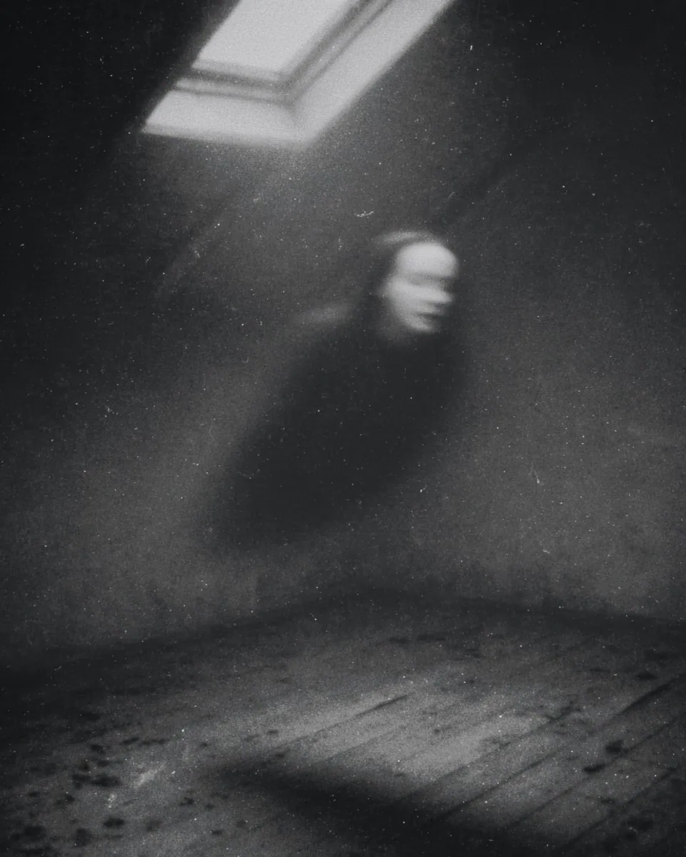 A blurred woman seems to float across an empty attic room beneath a skylight.