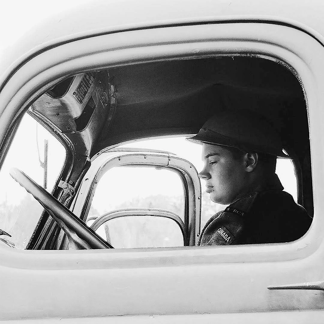 Black and white photograph of a young boy in a cap sitting quietly in the cab of a vintage truck