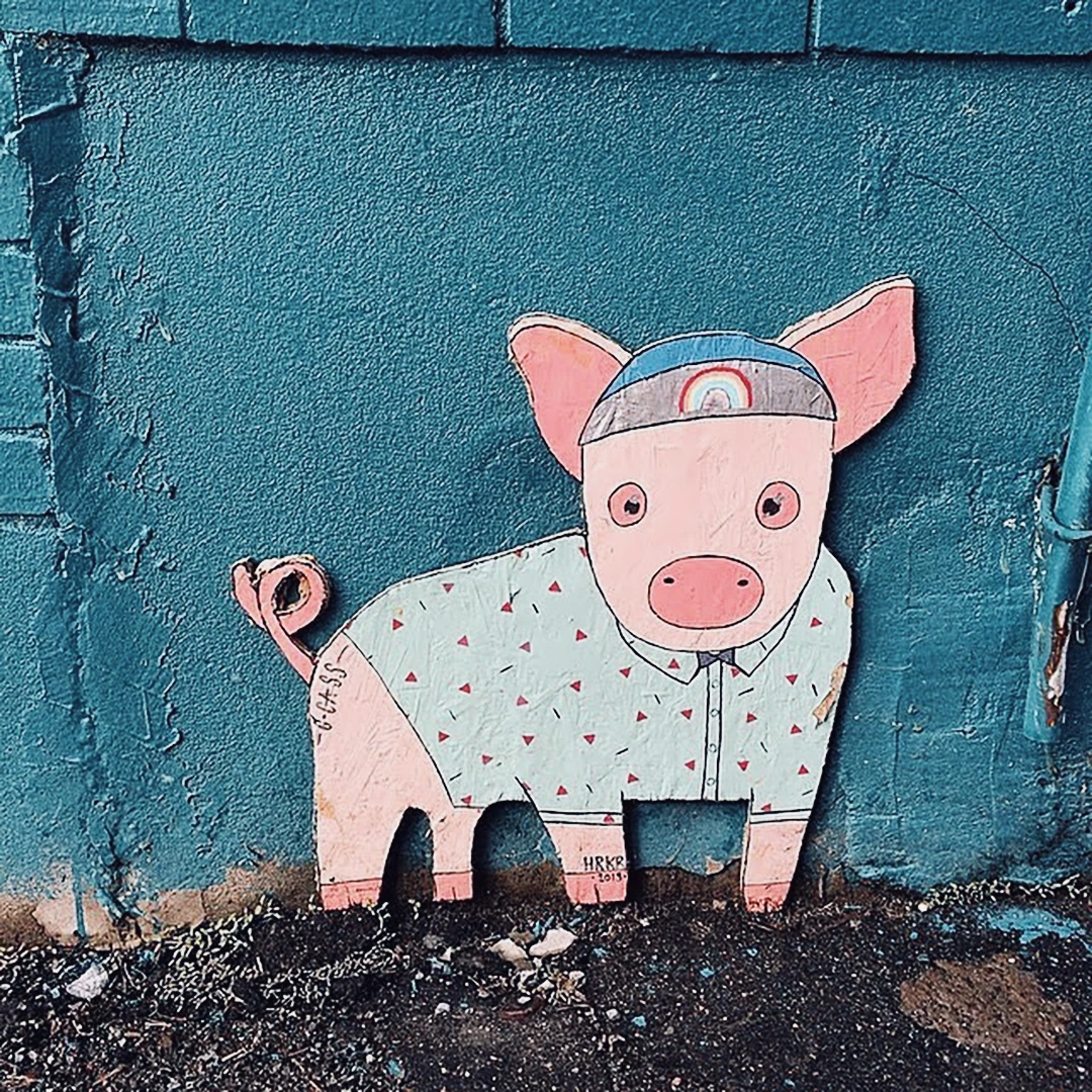 Street art of a pig wearing a floral shirt and baseball cap, painted on a teal wall