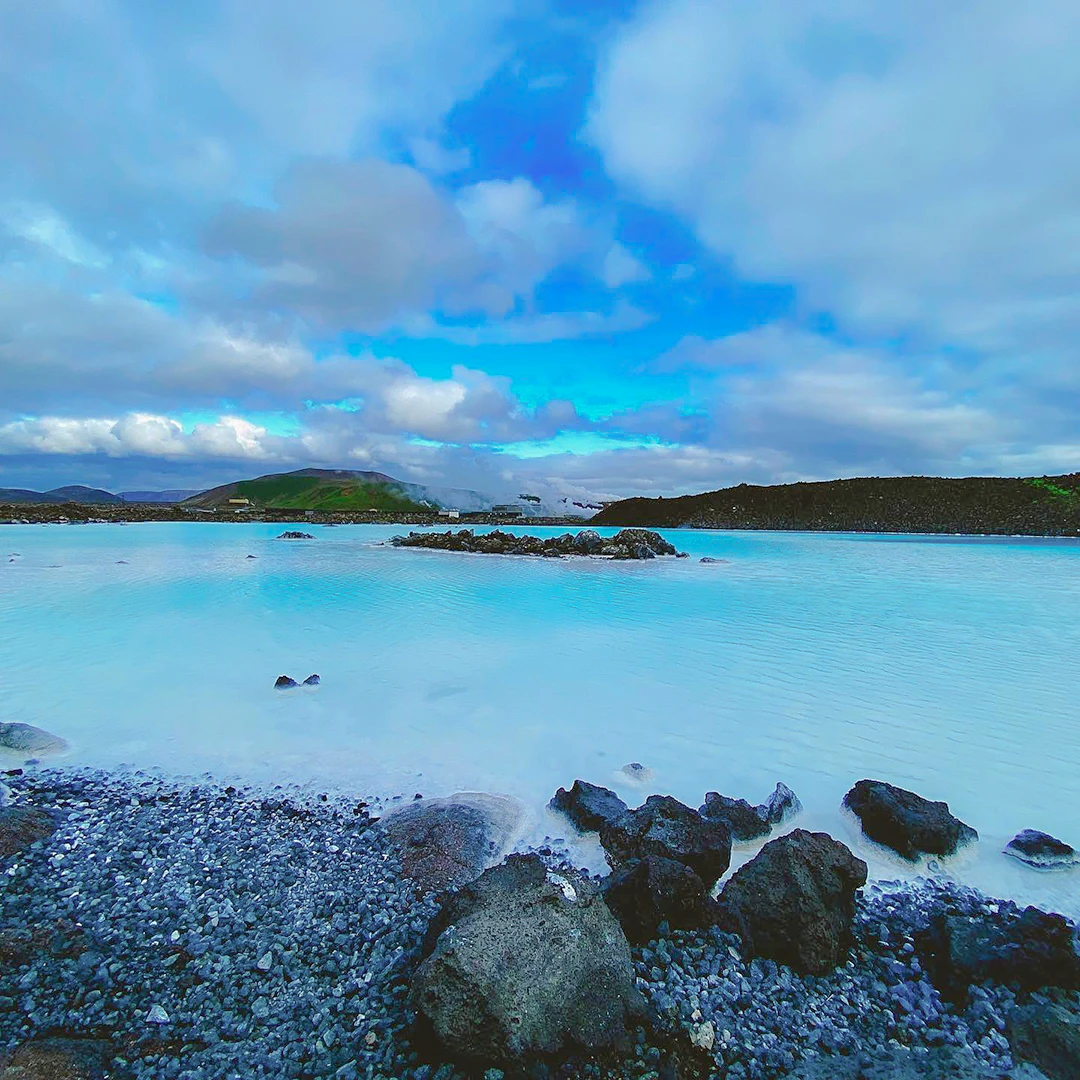 Milky blue geothermal waters of Iceland's Blue Lagoon stretching toward green hills under a dramatic cloudy sky
