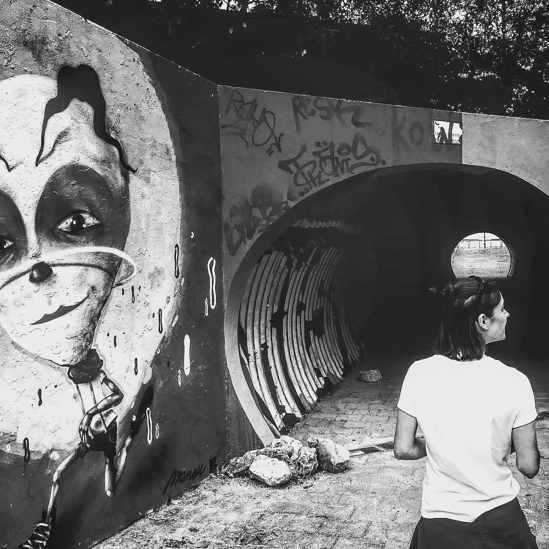 Black and white photo of a girl walking toward a graffiti tunnel featuring a large painted clown face