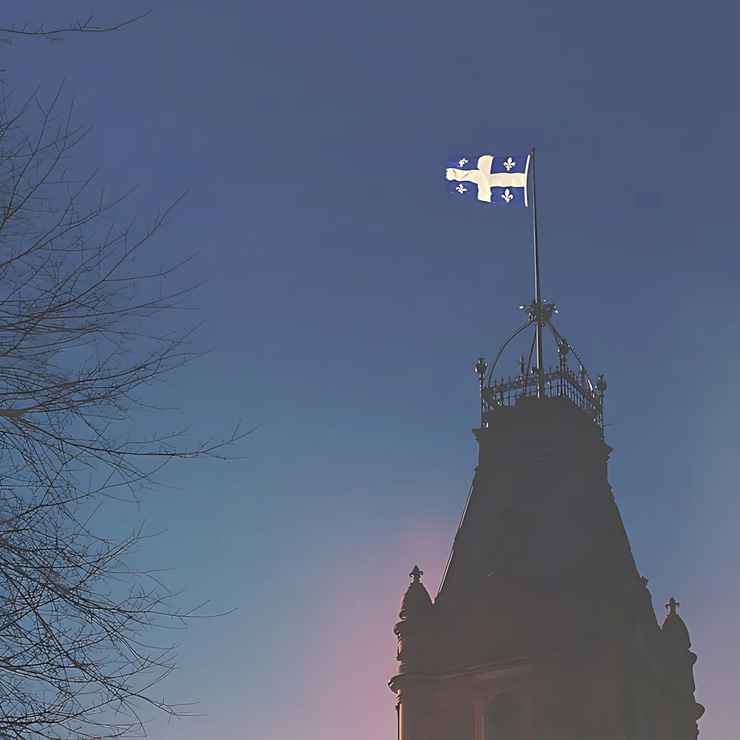 The Quebec flag flying from an ornate government tower at dusk, silhouetted against a gradient blue and pink sky