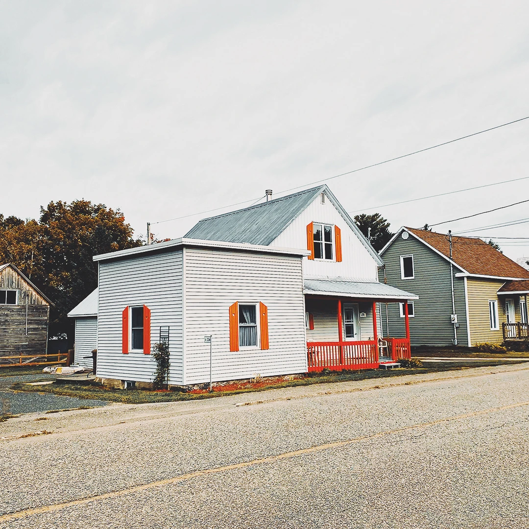 A small white clapboard house with vivid orange shutters and a red porch on a quiet residential street in autumn