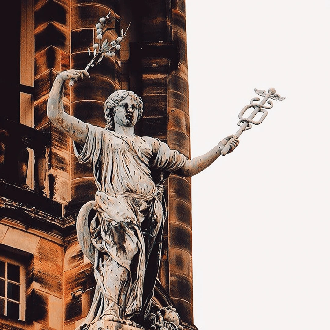 Stone statue of a classical goddess holding a caduceus and a bird, set against a grand ornate building facade
