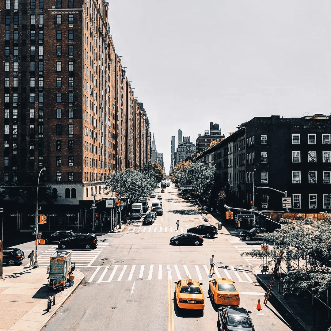 Looking down a wide New York City avenue lined with brick apartment buildings, yellow taxis at an intersection below
