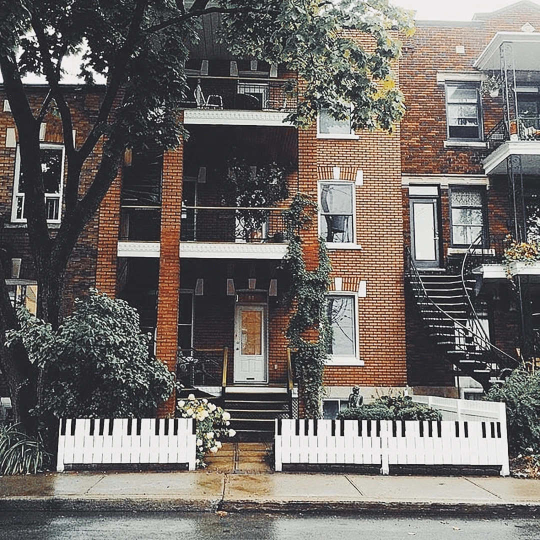 A Montreal brick duplex with a front fence painted as piano keys, spiral staircases and balconies draped in vines