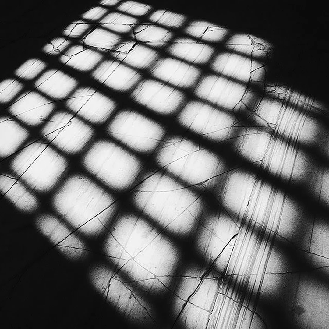 Black and white photograph of a grid-pattern window shadow cast across a cracked floor