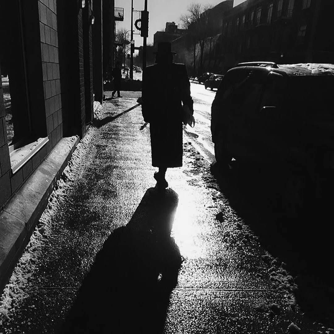 Black and white silhouette of a person walking on a wet winter sidewalk, long shadow stretching behind them