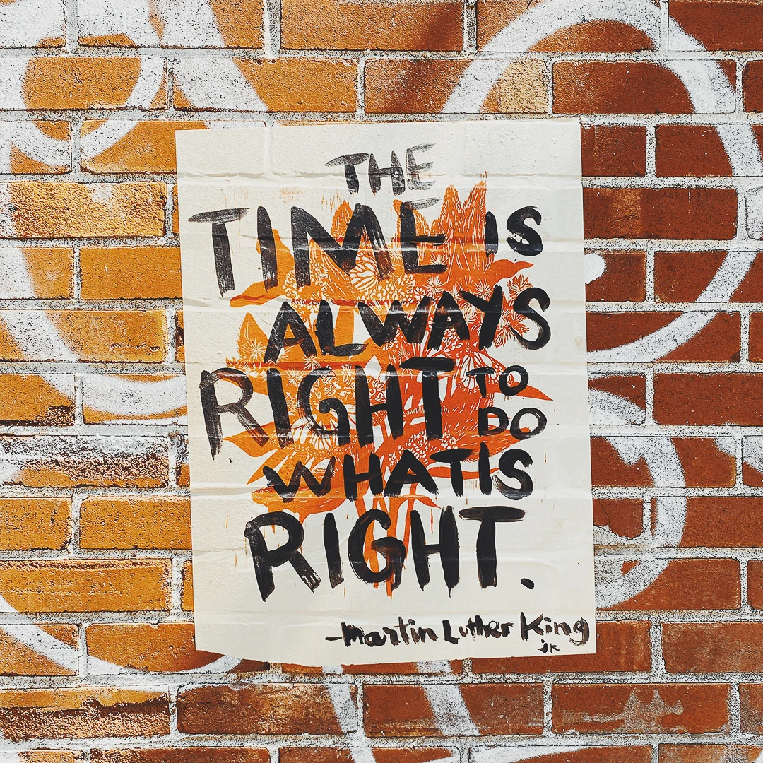 A hand-lettered poster on a graffiti brick wall reading The time is always right to do what is right, attributed to Martin Luther King Jr.