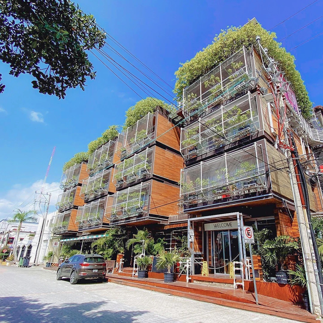 A multi-storey building with lush overflowing greenery and plants cascading from every balcony under a bright blue sky