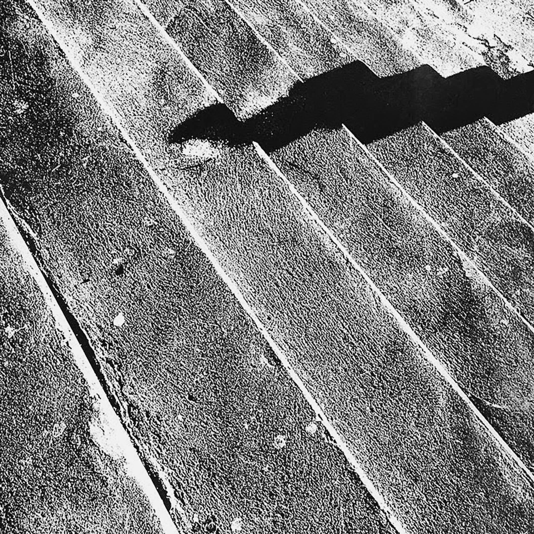 Black and white close-up of worn stone steps with deep diagonal shadows cutting across the surface