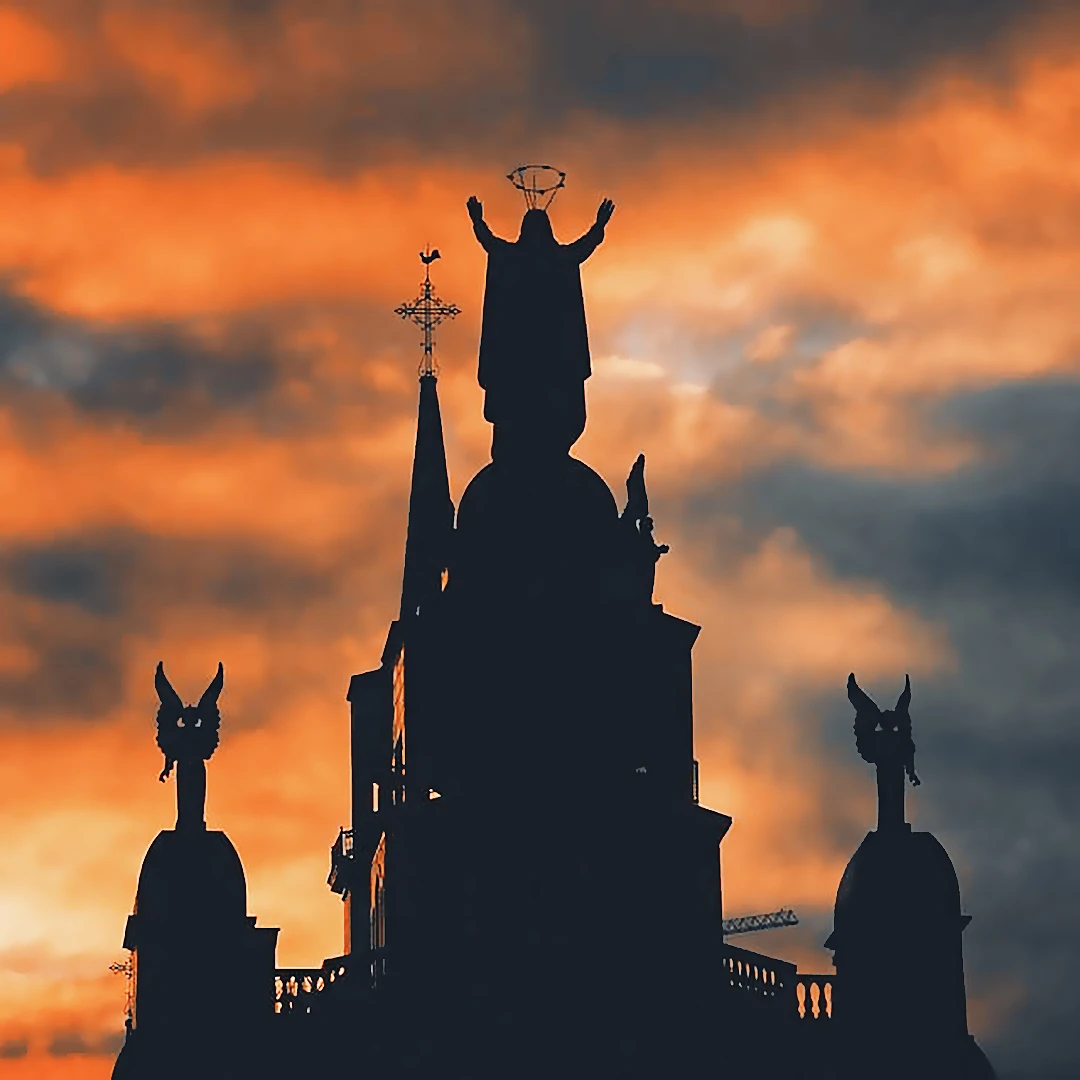 Silhouette of a cathedral rooftop with a Christ figure and flanking angels against a fiery orange sunset sky