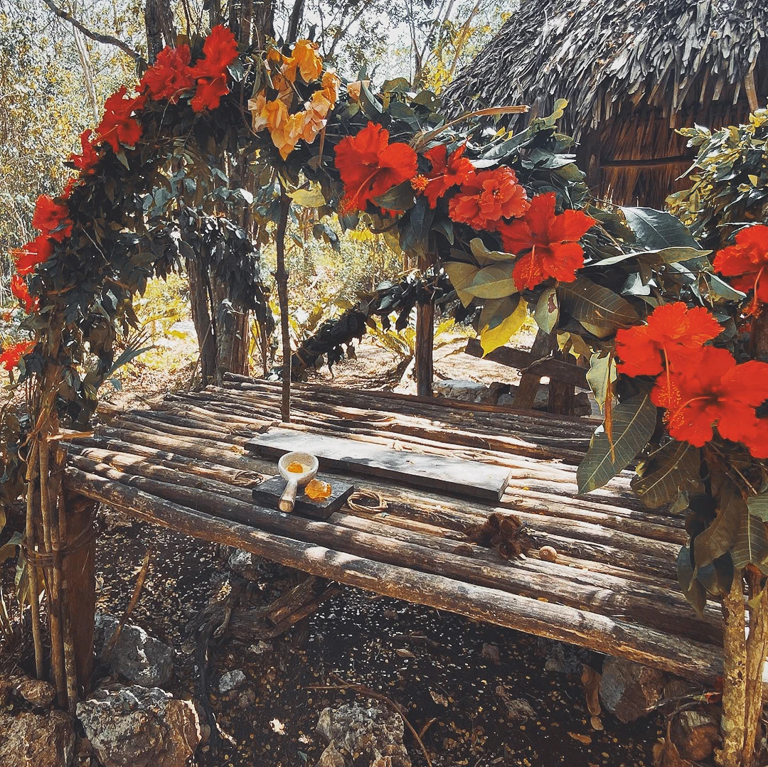 A rustic wooden altar decorated with bright red and orange tropical flowers in a shaded outdoor garden