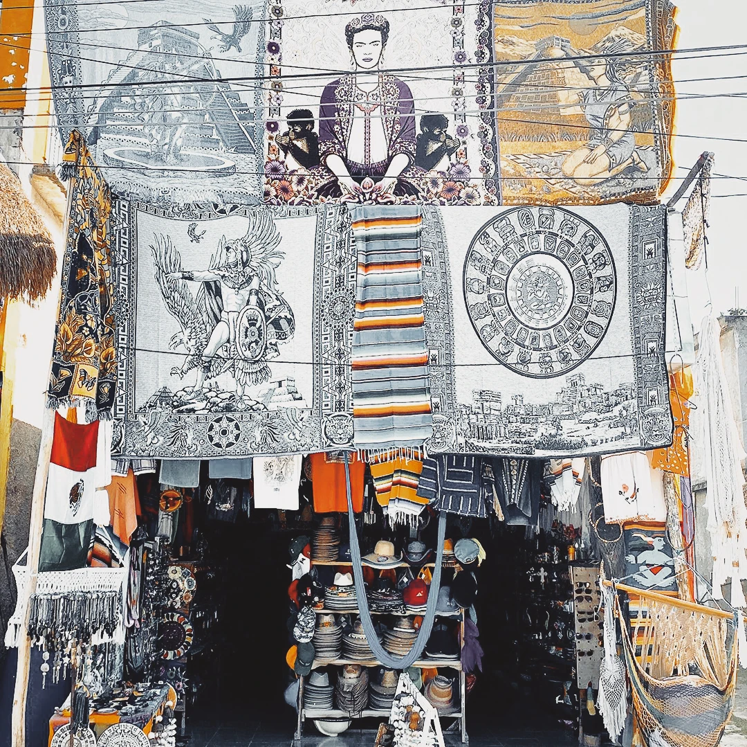 A Mexican market stall draped with colourful tapestries and textiles including a prominent Frida Kahlo portrait