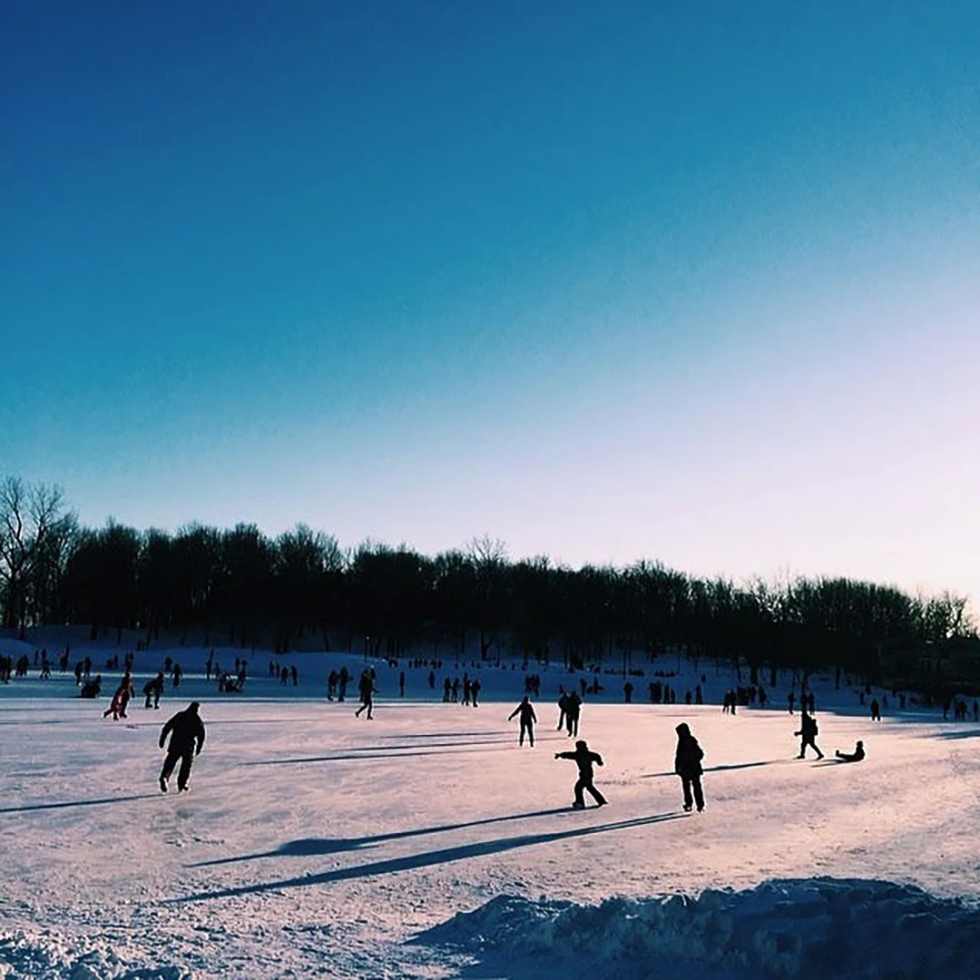 Silhouettes of people skating and playing on a frozen lake under a vast clear blue winter sky