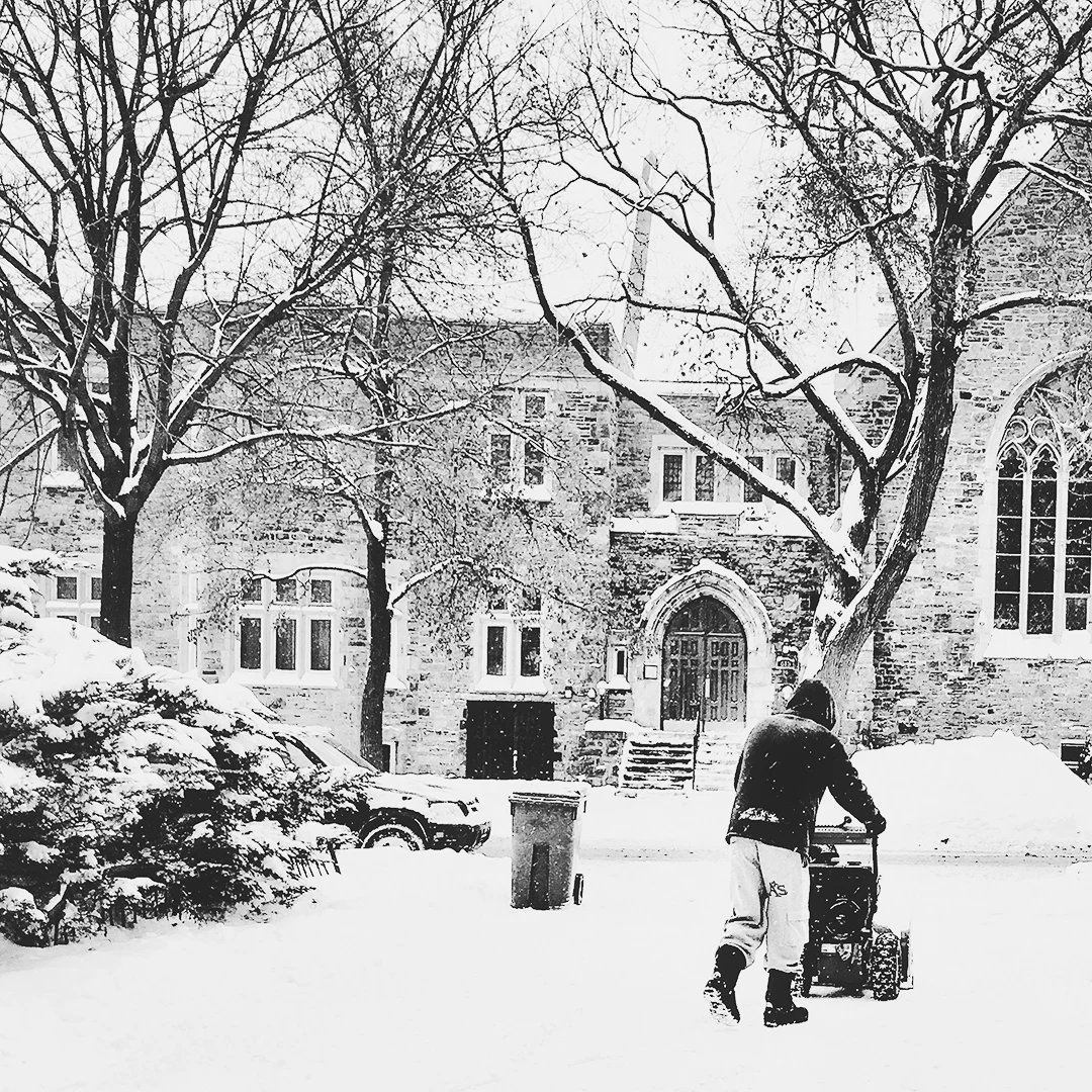 Black and white image of a person pushing a stroller through heavy snow toward a Gothic stone building